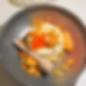 Panna cotta topped with orange flower and crunchy toffee pieces on a black plate with a honey dipper, create a vibrant dessert display.